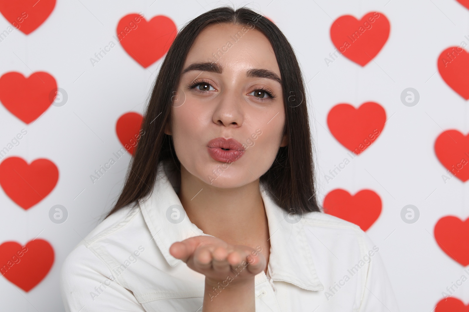 Photo of Young woman blowing kiss into camera on decorated background