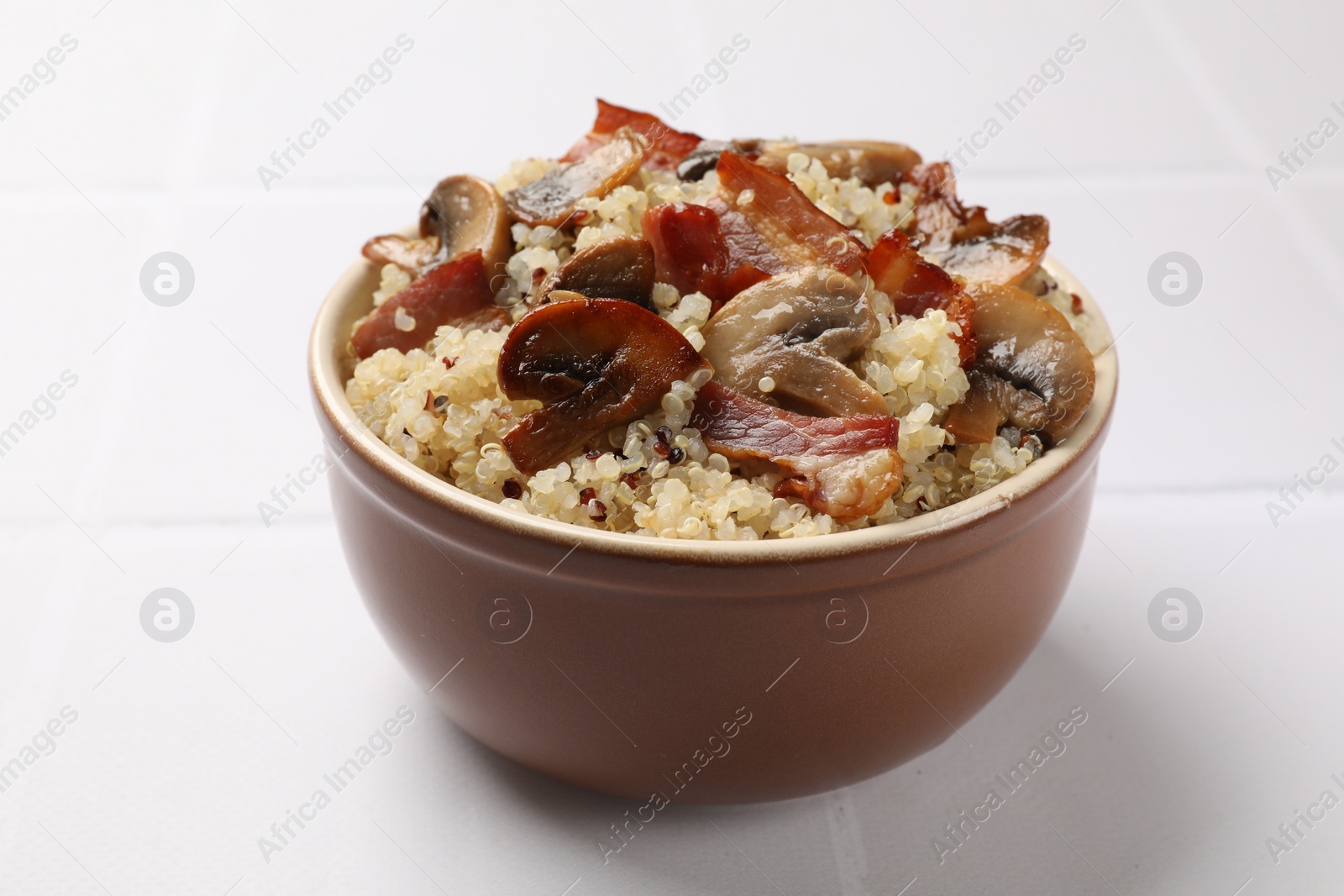 Photo of Tasty quinoa porridge with fried bacon and mushrooms in bowl on white table, closeup