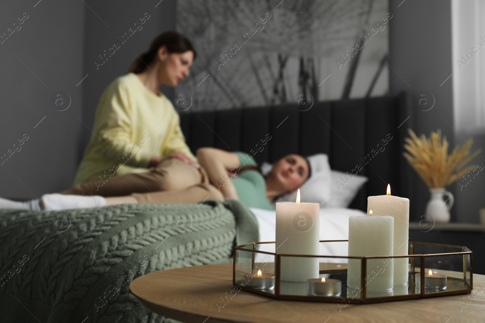 Photo of Doula working with pregnant woman in bedroom, focus on burning candles. Preparation for child birth