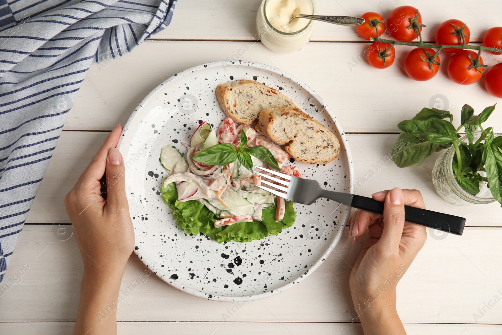 Photo of Top view of woman eating delicious vegetable salad with mayonnaise and croutons at white wooden table, closeup