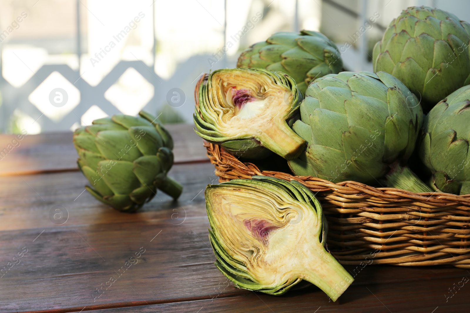 Photo of Wicker basket with fresh raw artichokes on wooden table. Space for text