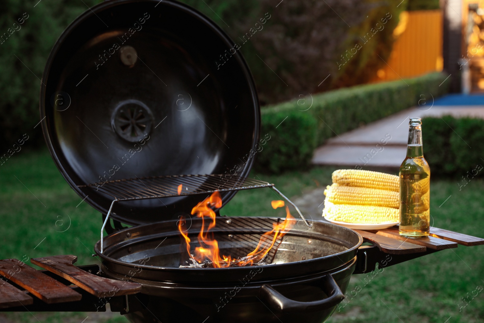 Photo of Barbecue grill with corn cobs and bottle of beer outdoors