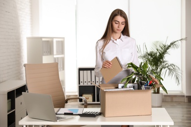 Photo of Upset young woman packing stuff in box at office