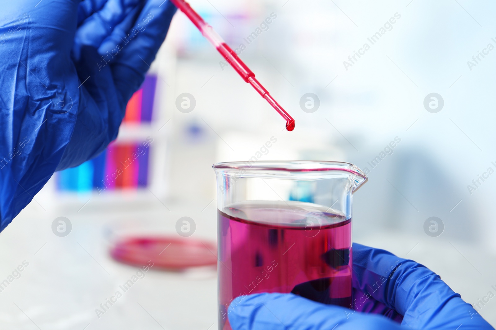 Photo of Scientist dripping reagent into beaker with sample in chemistry laboratory, closeup