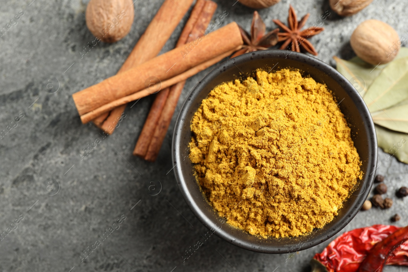 Photo of Dry curry powder in bowl and other spices on dark textured table, flat lay. Space for text