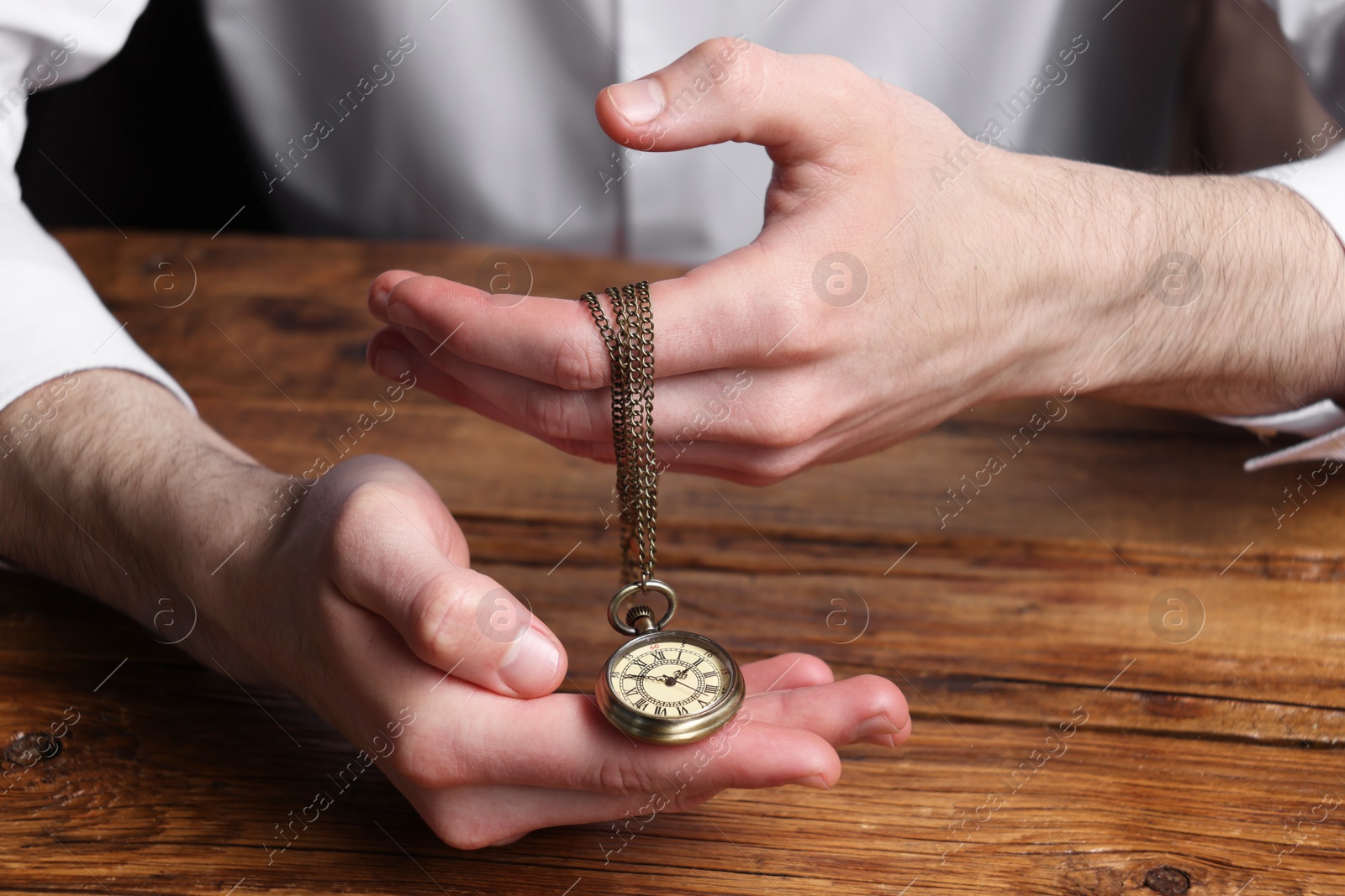 Photo of Man holding chain with elegant pocket watch at wooden table, closeup