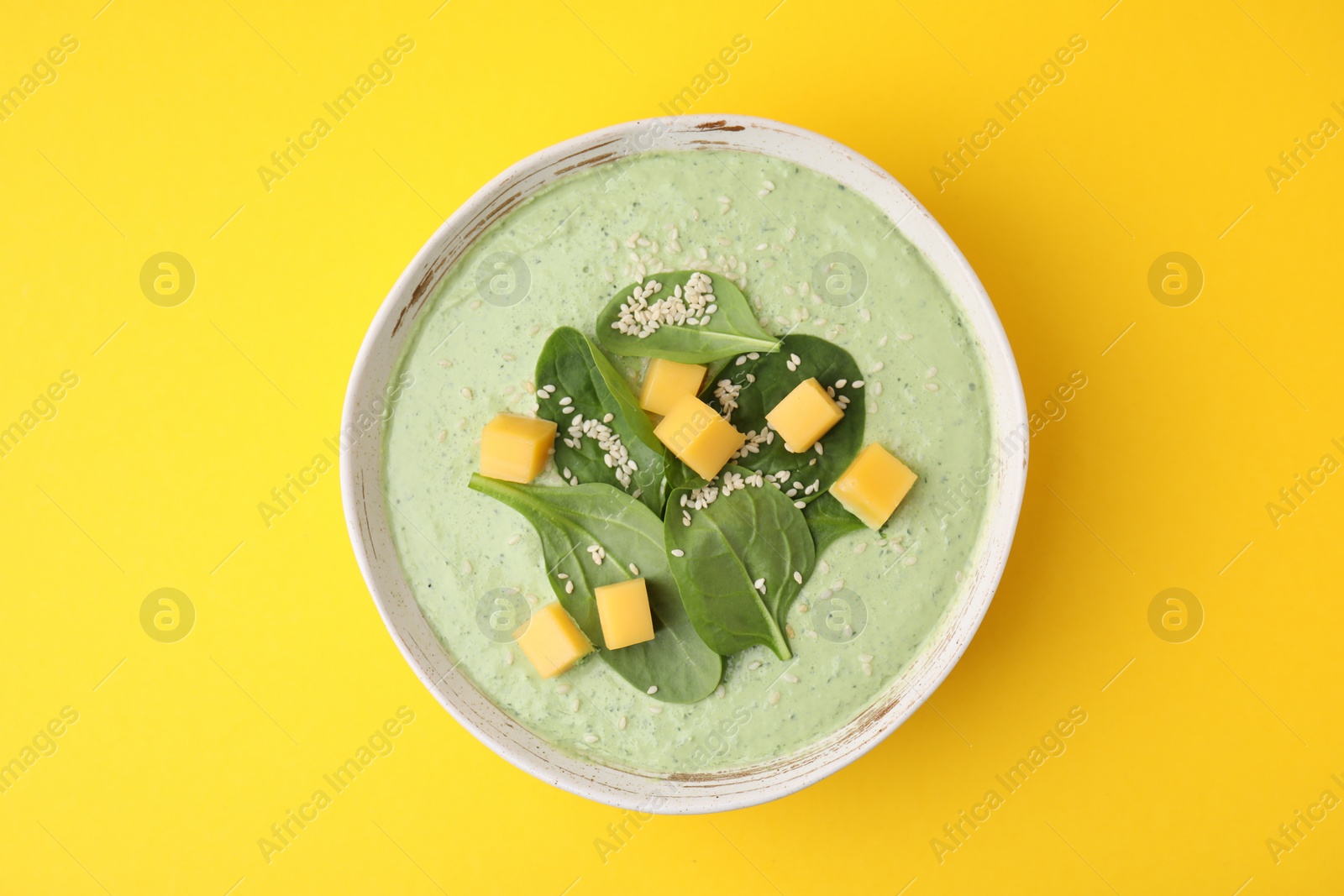 Photo of Delicious spinach cream soup with cheese in bowl on yellow background, top view