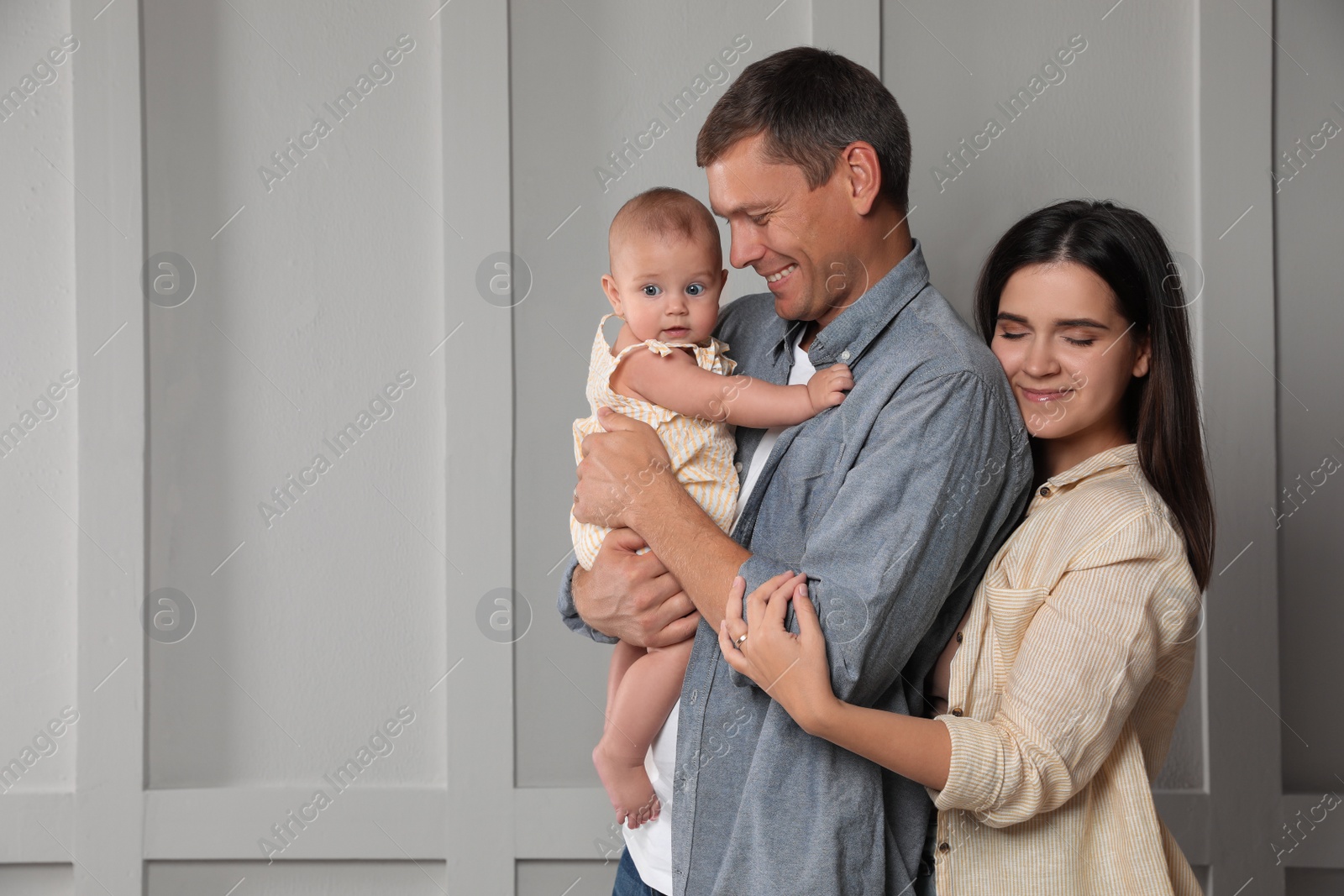 Photo of Happy family. Couple with their cute baby near light wall, space for text