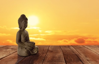 Beautiful stone Buddha sculpture on wooden surface at sunset. Space for text