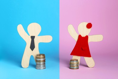 Photo of Gender pay gap. Wooden figures of man and woman with stacked coins on color background