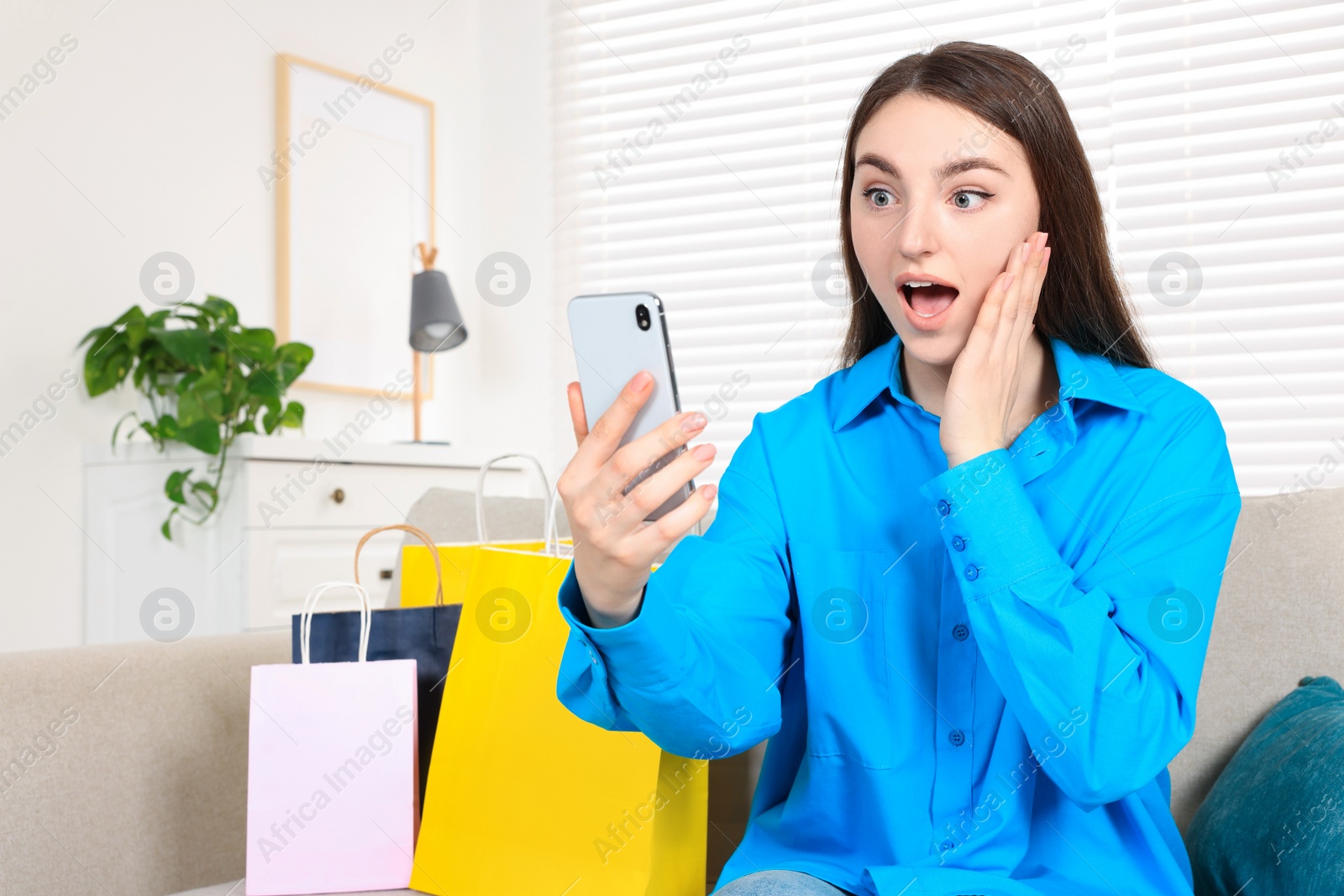 Photo of Special Promotion. Emotional young woman looking at smartphone on sofa indoors