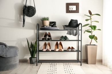 Black shelving unit with shoes and different accessories near white wall in hall