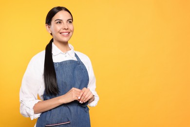 Young woman in blue jeans apron on yellow background, space for text