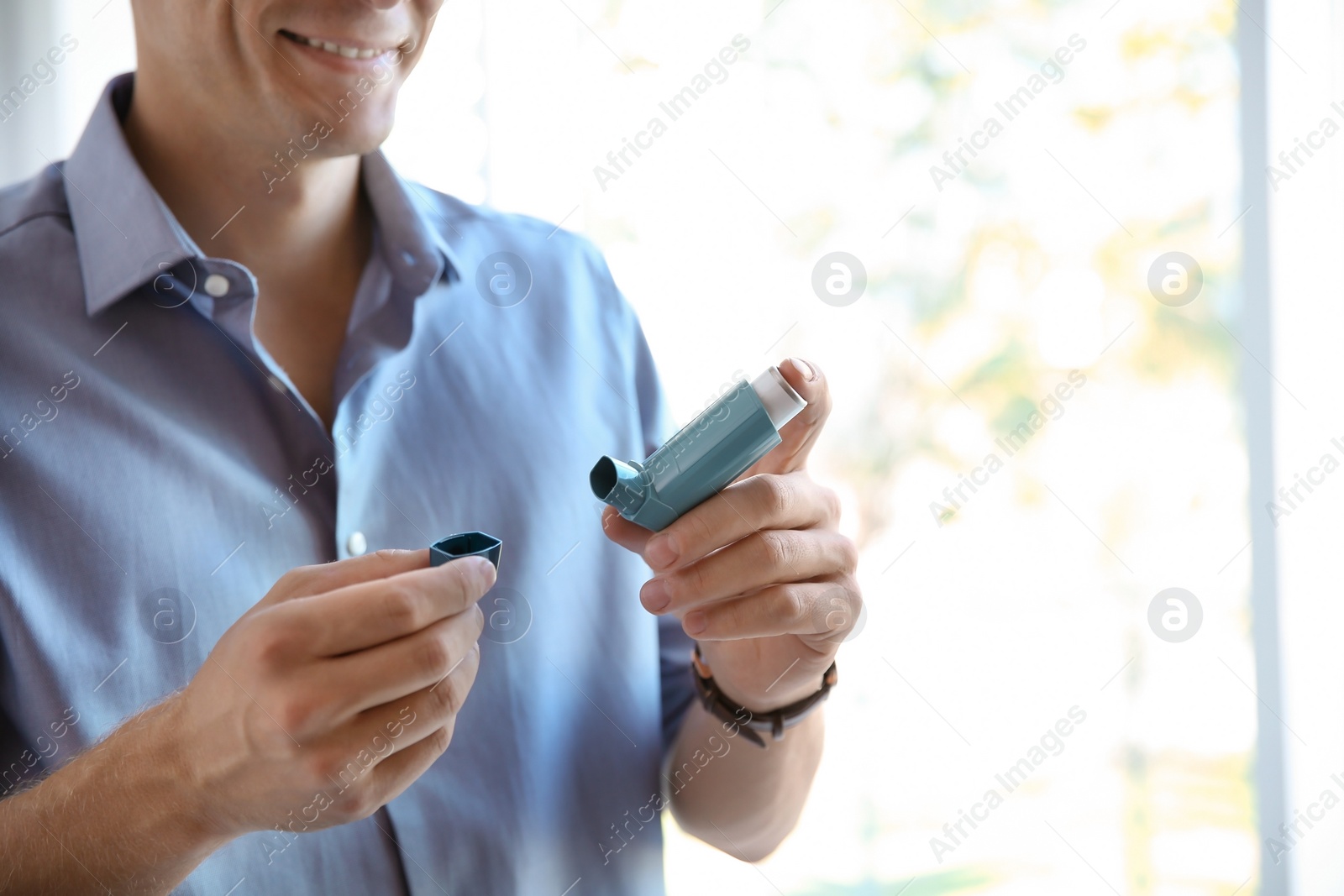 Photo of Young man with asthma inhaler indoors, closeup. Space for text