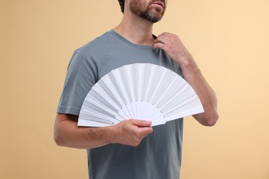 Man holding hand fan on beige background, closeup