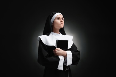 Photo of Young nun with Bible on black background