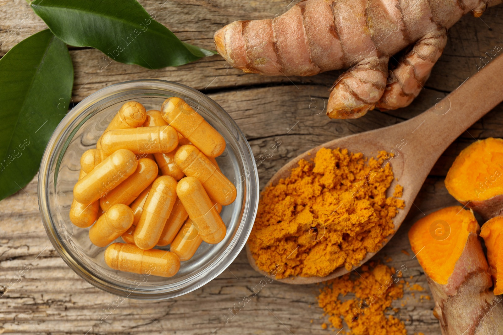 Photo of Aromatic turmeric powder, raw roots and pills on wooden table, flat lay