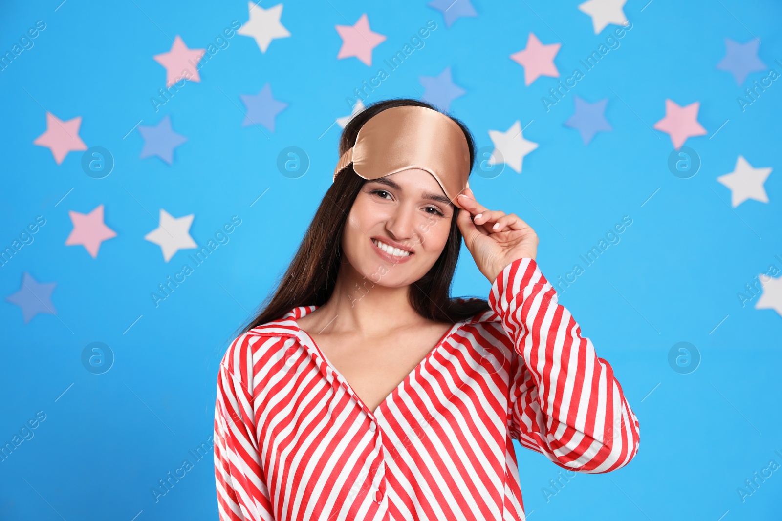 Photo of Beautiful woman wearing sleeping mask on light blue background. Bedtime