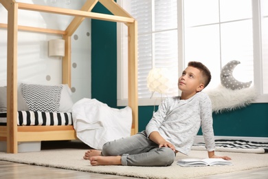 Little boy with book in stylish bedroom interior