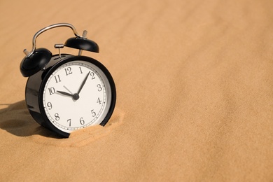 Photo of Black alarm clock on sand in desert. Space for text