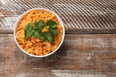 Photo of Delicious red lentils with parsley in bowl on wooden table, top view. Space for text