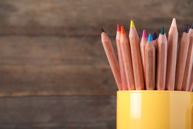 Colorful pencils in cup on wooden background, closeup. Space for text