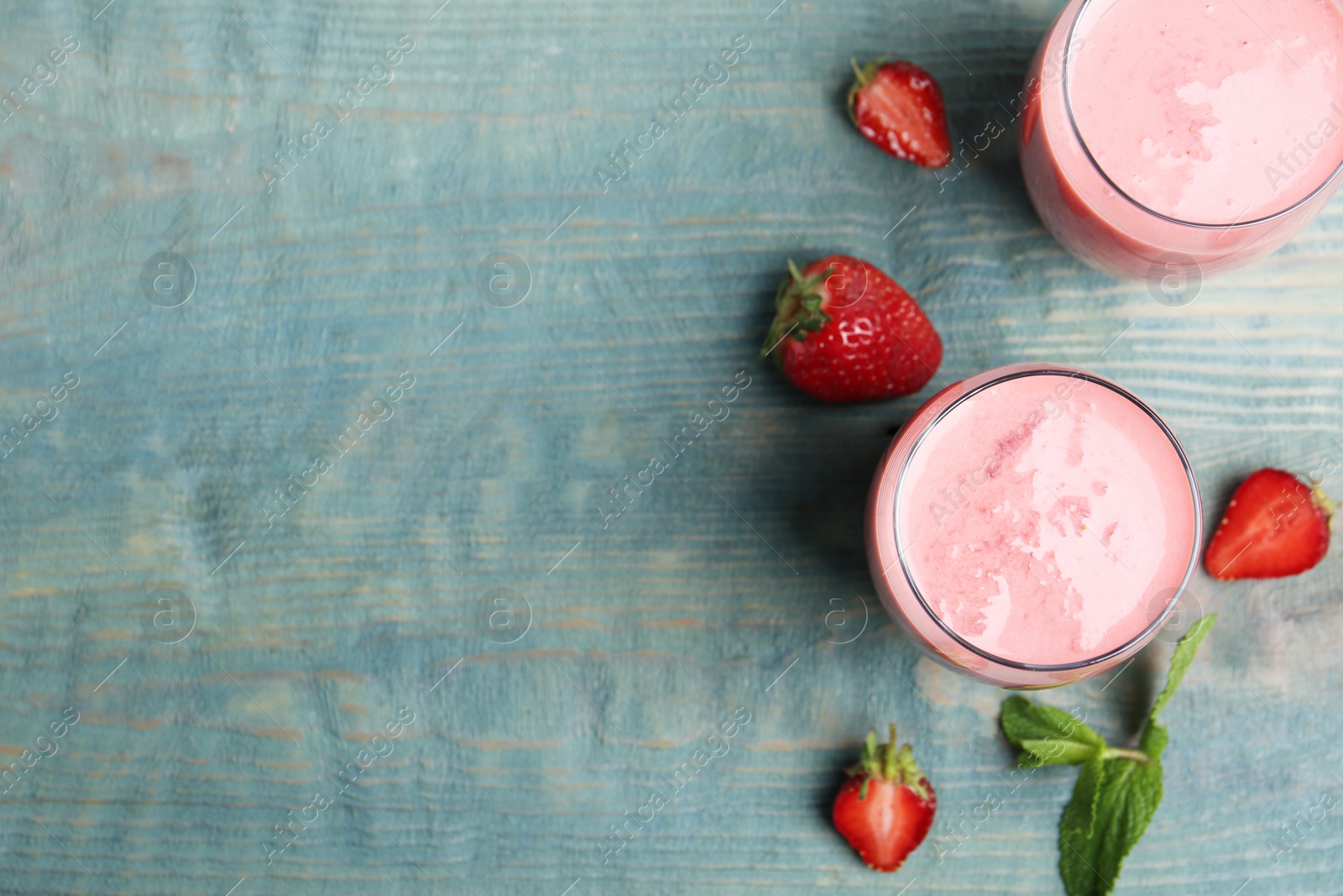 Photo of Tasty strawberry smoothies in glasses on blue wooden table, flat lay. Space for text