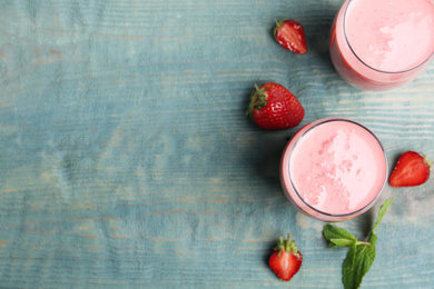 Photo of Tasty strawberry smoothies in glasses on blue wooden table, flat lay. Space for text