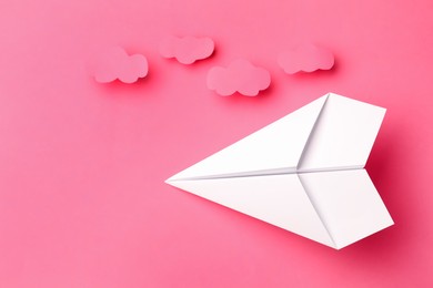 Photo of Handmade white paper plane with clouds on pink background, flat lay. Space for text