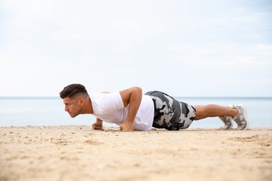 Photo of Muscular man doing push up on beach. Body training