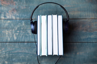 Modern headphones with hardcover books on wooden table, top view