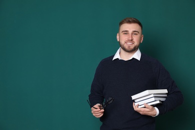 Portrait of young teacher with books and glasses on green background. Space for text