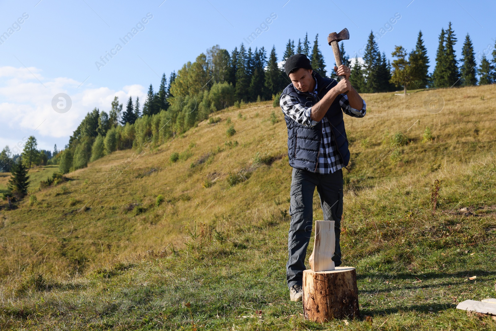 Photo of Handsome man with axe cutting firewood on hill