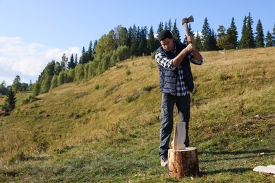 Handsome man with axe cutting firewood on hill