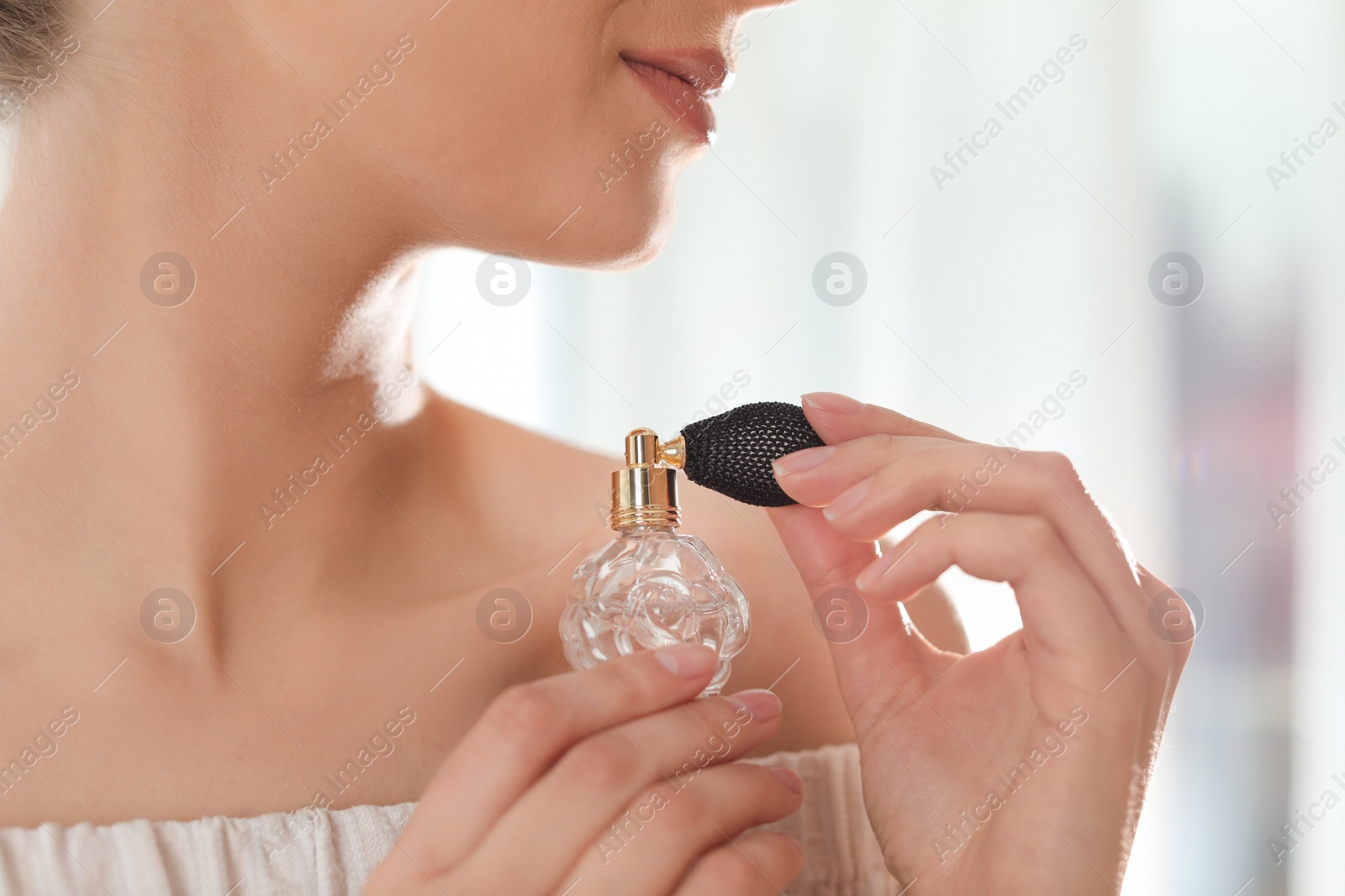 Photo of Young woman with bottle of perfume on blurred background, closeup