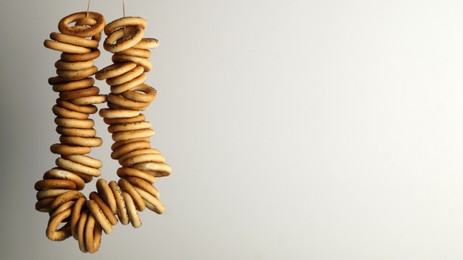 Photo of Bunch of delicious ring shaped Sushki (dry bagels) hanging on light grey background. Space for text