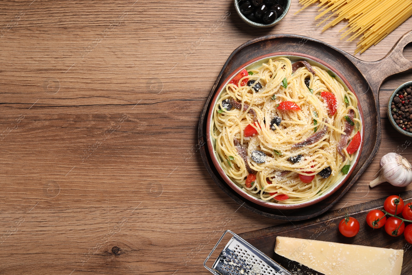 Photo of Plate of delicious pasta with anchovies and ingredients on wooden table, flat lay. Space for text