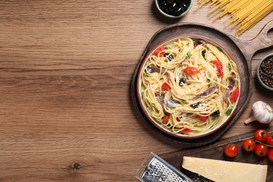 Photo of Plate of delicious pasta with anchovies and ingredients on wooden table, flat lay. Space for text