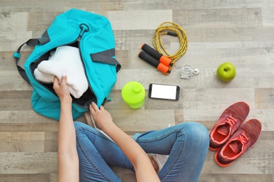 Young woman packing sports bag on floor, top view