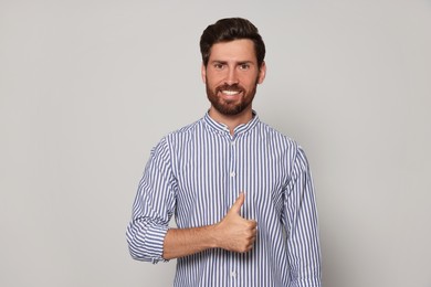 Handsome bearded man showing thumb up on light grey background