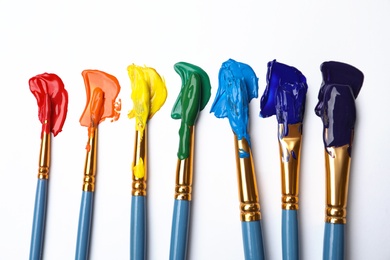Photo of Set of brushes with different paints on white background, flat lay. Rainbow colors