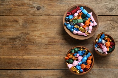 Photo of Candies in colorful wrappers on wooden table, flat lay. Space for text