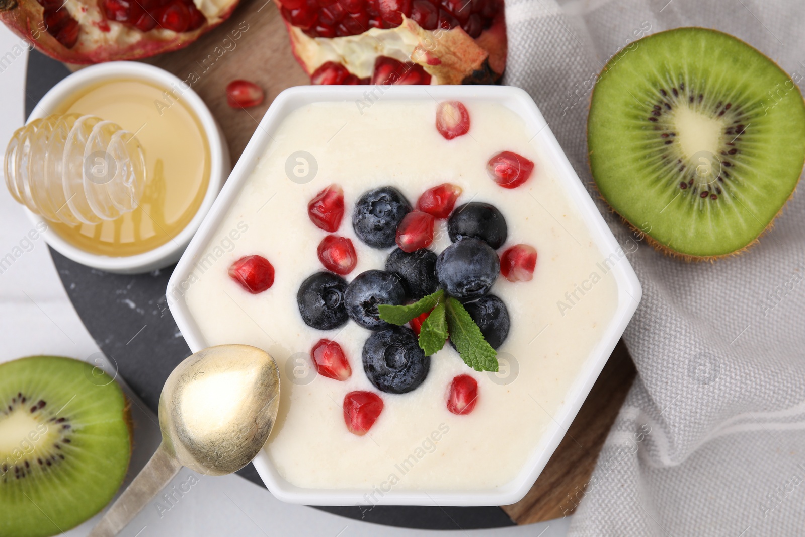 Photo of Bowl of delicious semolina pudding with blueberries, pomegranate and mint served on table, flat lay