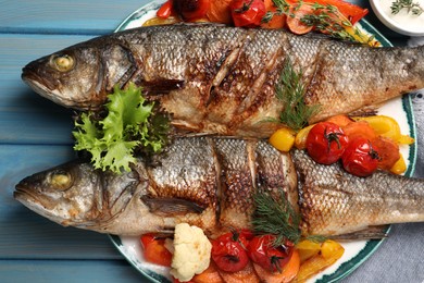 Photo of Plate with delicious roasted sea bass fish and vegetables on light blue table
