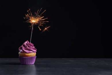Photo of Delicious birthday cupcake with sparkler on table against black background