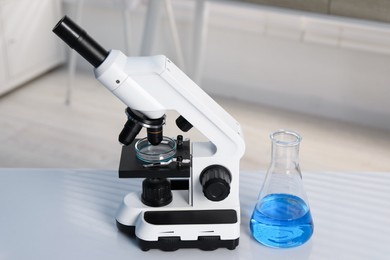 Photo of Laboratory analysis. Flask with blue liquid, petri dish and microscope on white table indoors