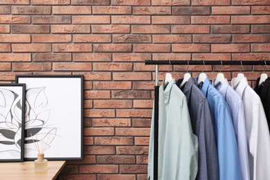 Photo of Wardrobe rack with stylish clothes near brick wall in dressing room