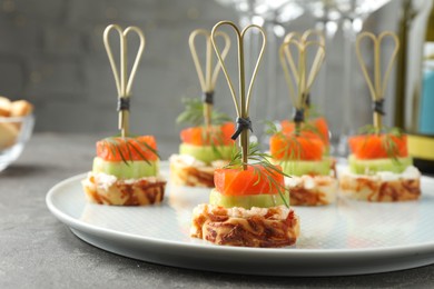 Photo of Tasty canapes with salmon, cucumber, bread and cream cheese on grey table, closeup