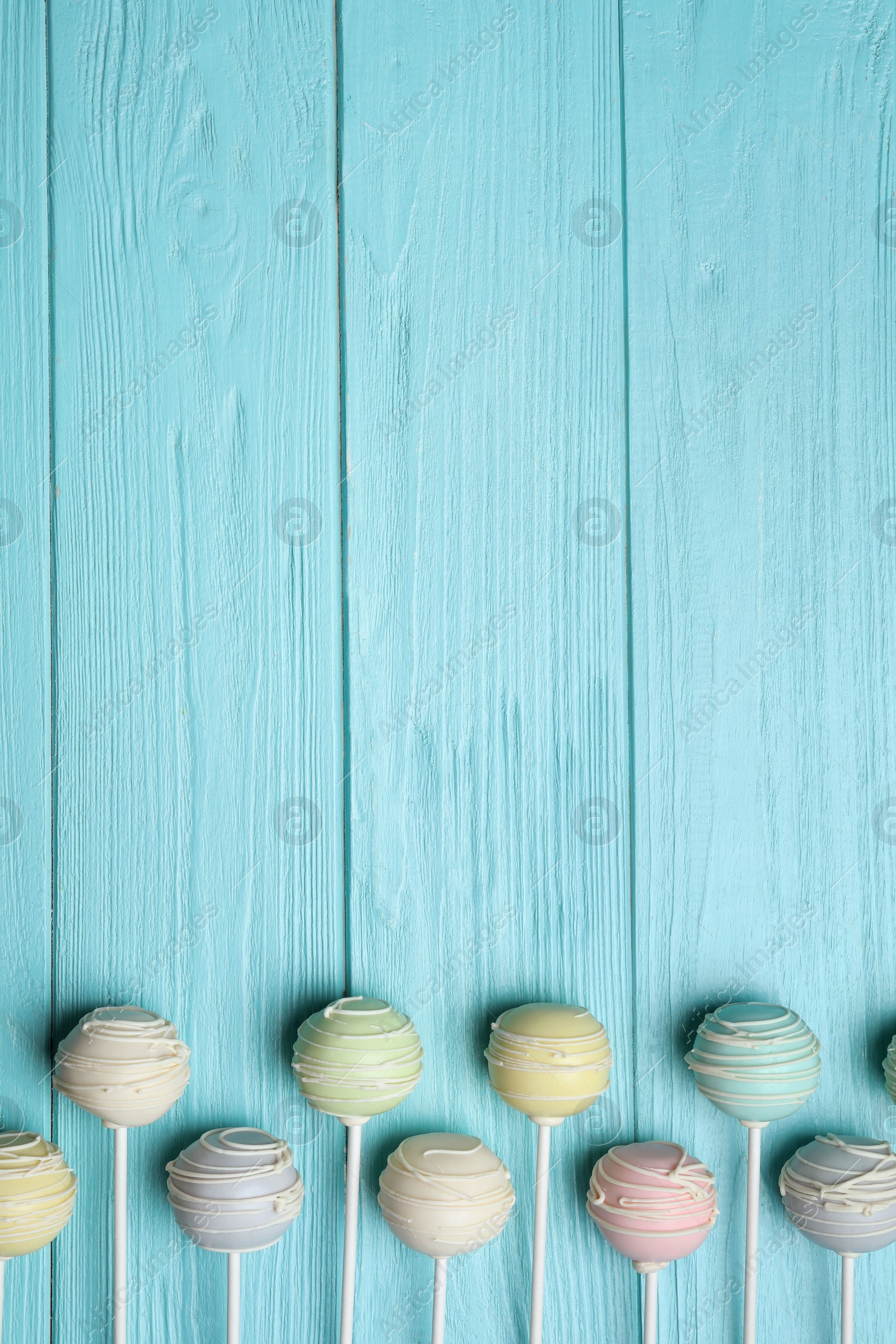 Photo of Sweet colorful cake pops on turquoise wooden background, flat lay. Space for text