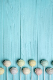 Sweet colorful cake pops on turquoise wooden background, flat lay. Space for text